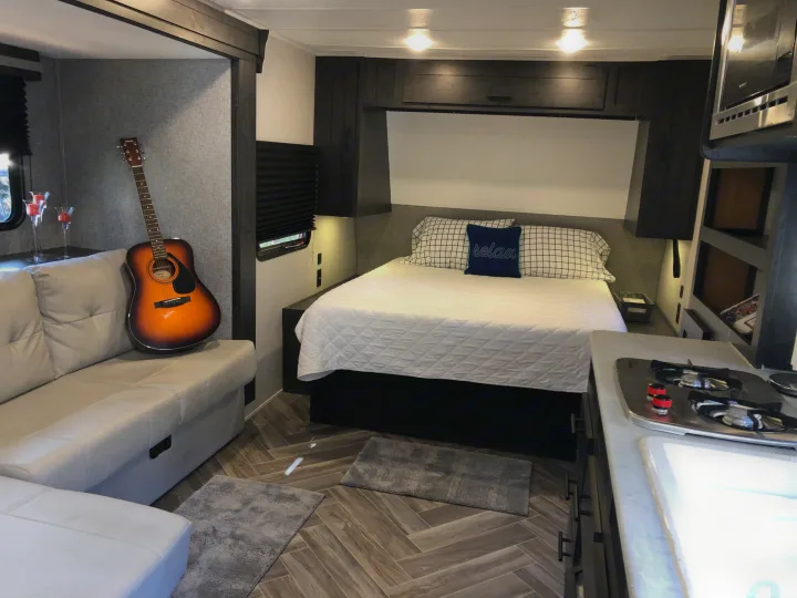 Explore this modern RV rental interior featuring a comfy sofa, bedroom with 'relax' pillow, and functional kitchenette.. Forest River Ozark 1800 QS 2020