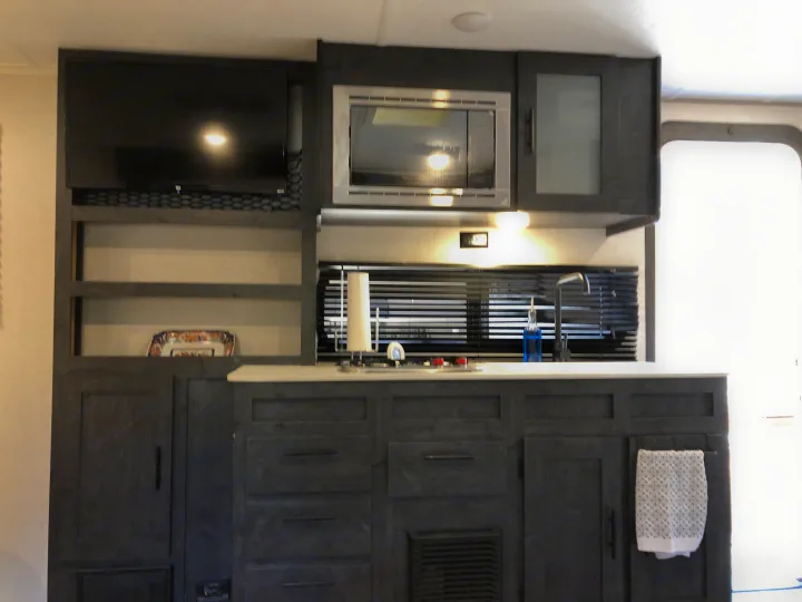 Compact modern RV rental kitchen with TV, microwave, sink, and ample storage for your travels.. Forest River Ozark 1800 QS 2020