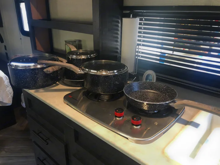 RV rental kitchen: black speckled pots & pans on a two-burner stove, ready for delicious road trip cooking!. Forest River Ozark 1800 QS 2020