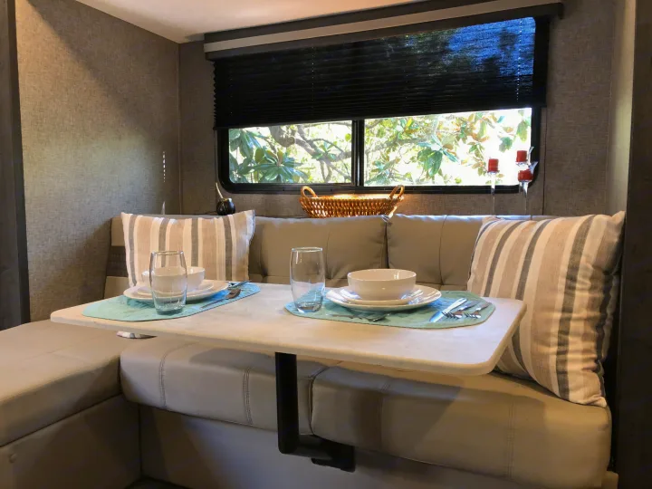 Cozy RV rental dinette with U-shaped seating, a set table, and a scenic window view, ideal for meals on the go.. Forest River Ozark 1800 QS 2020