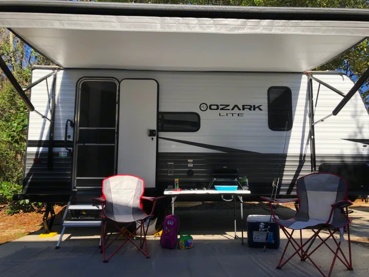 Spacious RV rental, 'Ozark Lite' travel trailer, set up with awning, chairs, grill, cooler, and fishing gear for outdoor living.. Forest River Ozark 1800 QS 2020