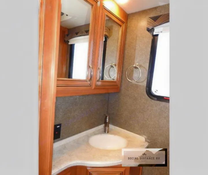 This RV rental features a compact bathroom vanity with a corner sink, mirrored cabinets, and a window.. Thor Motor Coach Venetian 2017