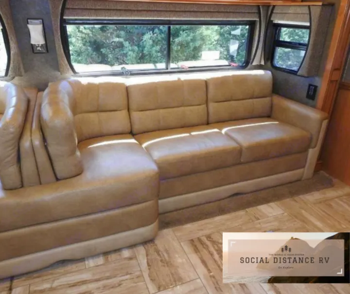 Spacious RV rental interior featuring a light brown L-shaped leather sofa, large windows, and wood-look floor. Ideal for travel.. Thor Motor Coach Venetian 2017