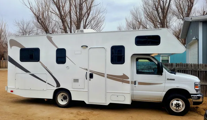 This white Class C RV rental, featuring brown stripes, is parked on a dirt lot, ready for your next adventure.. Thor Majestic 2017
