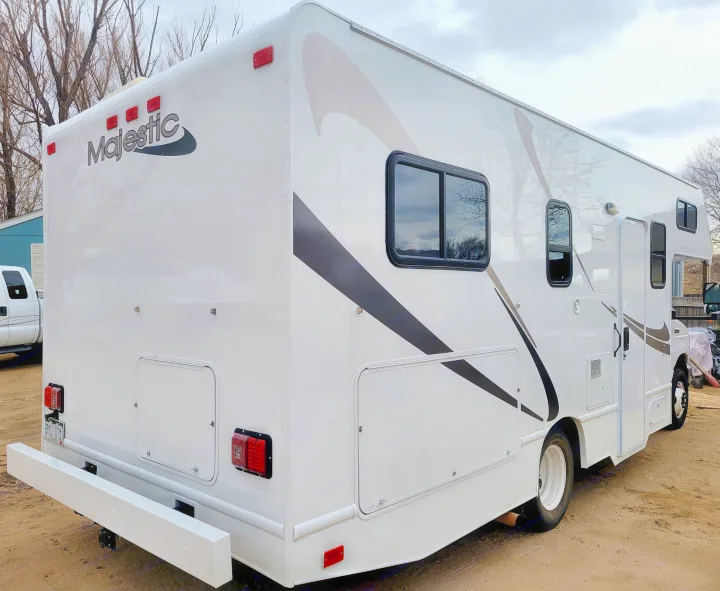 Clean white Majestic RV rental motorhome parked outdoors on dirt, showing its rear and side. A Class C recreation vehicle.. Thor Majestic 2017