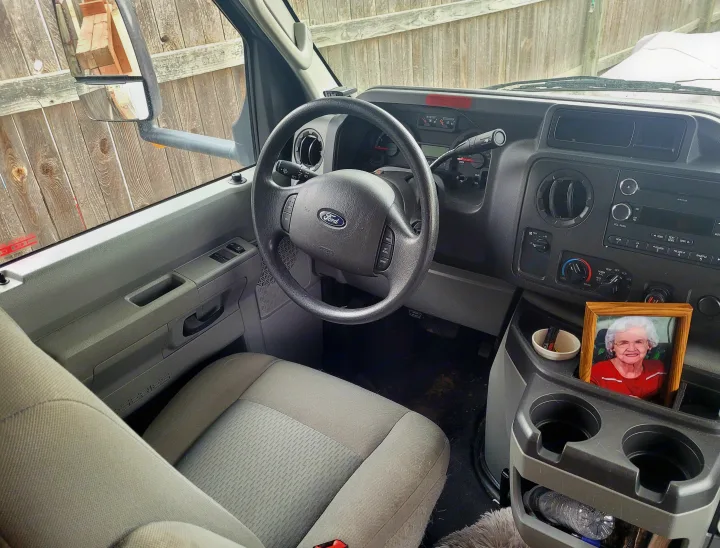 Interior of an E-Series rv rental, showing the driver's area with steering wheel, dashboard, and a console holding a framed photo.. Thor Majestic 2017