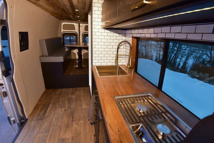 Step inside this inviting rv rental. Cozy camper van interior with wood floors, modern kitchen, and dining area.. Mercedes-Benz Sprinter 2021