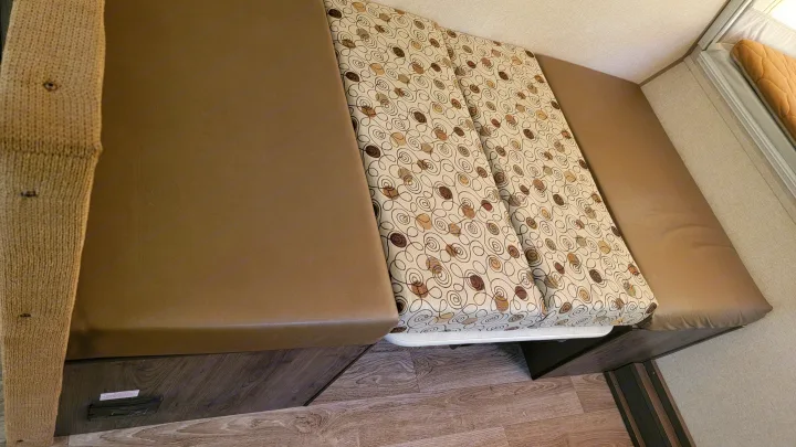 Inside an RV rental, two brown upholstered benches frame a patterned cushion, forming a convertible dinette.. Forest River Other 2019