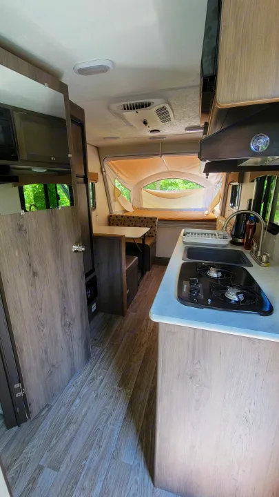 RV rental interior: a compact kitchenette with stove & sink, leading to a bright pop-up camper bed area.. Forest River Other 2019