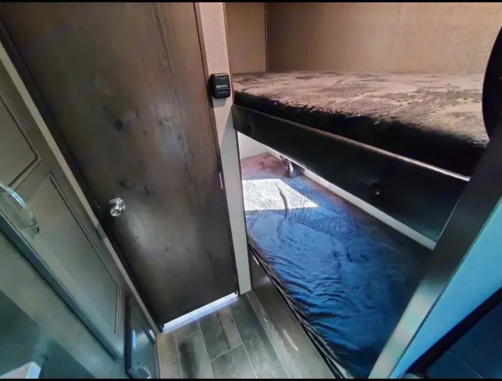 RV rental interior showing bunk beds with gray and blue bedding, a side control panel, and wood-toned finishes.. Jayco Jay Flight 2021