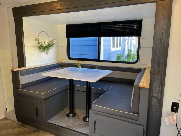 Cozy RV rental dinette with modern gray U-shaped seating, a white marble table, and large window. Compact mobile living.. Forest River 178BHSKX 2022
