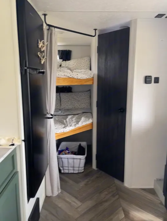 This compact RV rental interior features cozy bunk beds, a refrigerator, and a privacy curtain. Ideal for family adventures.. Forest River 178BHSKX 2022