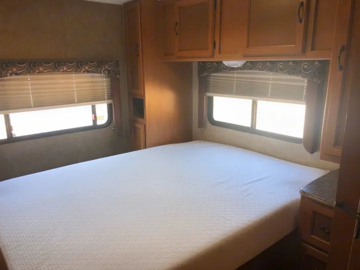 Inside an RV rental: cozy bedroom featuring a comfortable white bed, windows with blinds, and storage cabinets.. Coachmen Freelander 2014