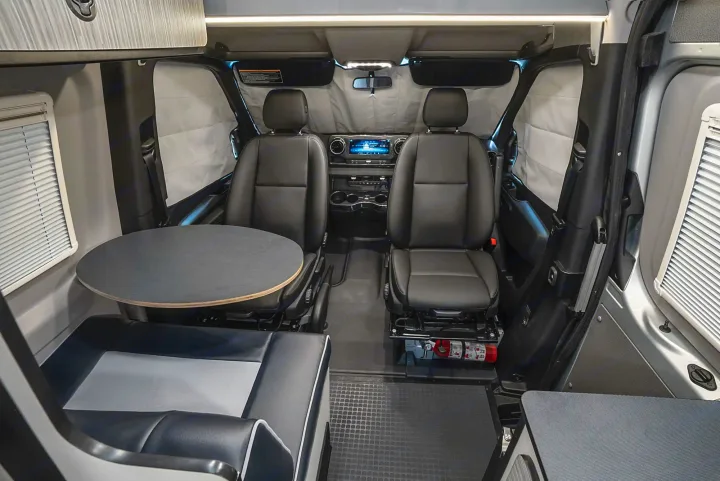 Inside an RV rental: Compact interior showing the driver's cabin with two seats and a rear dining area with a round table.. Winnebago Revel 2022