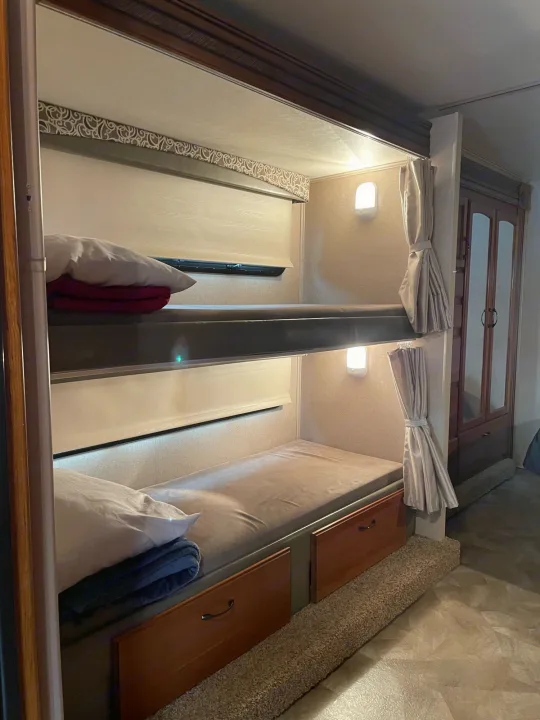 RV rental interior featuring two bunk beds with bedding, reading lights, and under-bed storage drawers.. Jayco Redhawk 2016