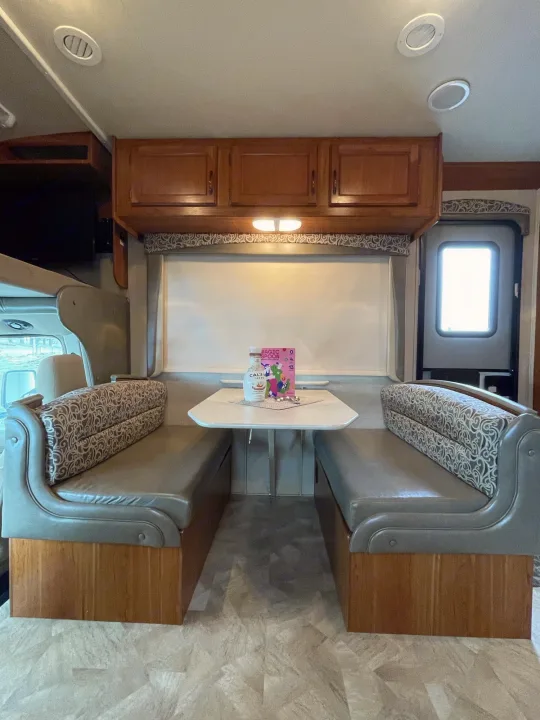 Interior view of an RV rental: a comfy dinette with grey benches, white table, and wood cabinets. Perfect for travel!. Jayco Redhawk 2016
