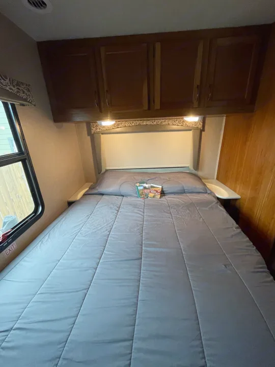 Cozy RV rental bedroom features a comfortable bed, emergency exit window, and overhead storage cabinetry.. Jayco Redhawk 2016