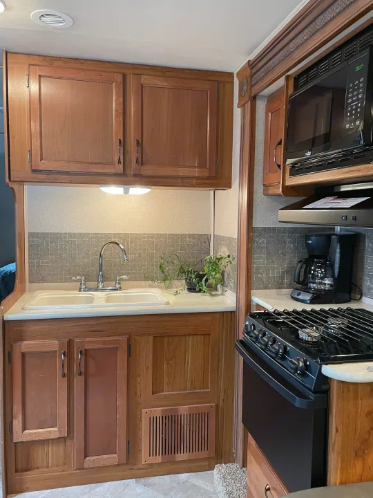 An RV rental kitchen featuring warm cherry wood cabinets, a double sink, built-in microwave, and gas stove.. Jayco Redhawk 2016