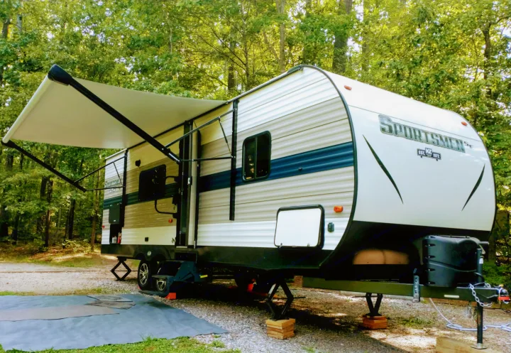 Enjoy this RV rental at a serene campsite. A Sportsmen travel trailer with awning deployed, ready for your camping adventures.. KZ Sportsmen 2021