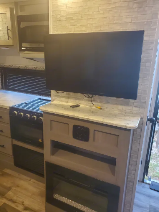Interior of an RV rental, showing a kitchen with a stove, microwave, and a living area with a TV and electric fireplace.. Coleman 2455bh 2022