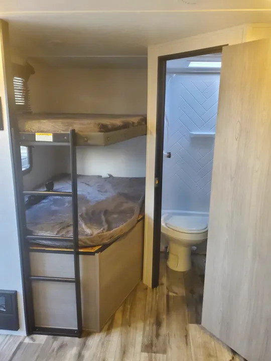RV rental interior: bunk beds with ladder on left, compact bathroom with toilet and herringbone shower on right.. Coleman 2455bh 2022