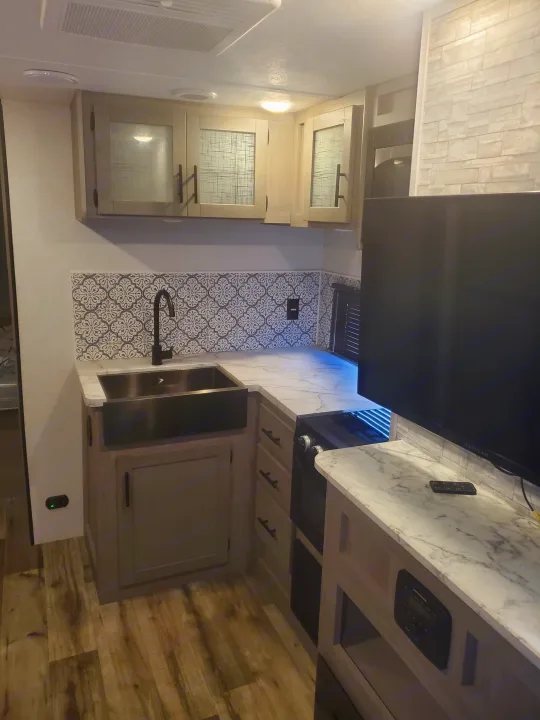Modern RV rental kitchen featuring a large sink, gas stove, sleek cabinets, and stylish backsplash for comfortable travel.. Coleman 2455bh 2022