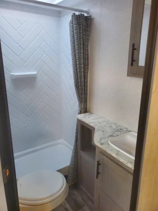 RV rental bathroom: modern design with a herringbone shower, toilet, and marble-top vanity with sink.. Coleman 2455bh 2022