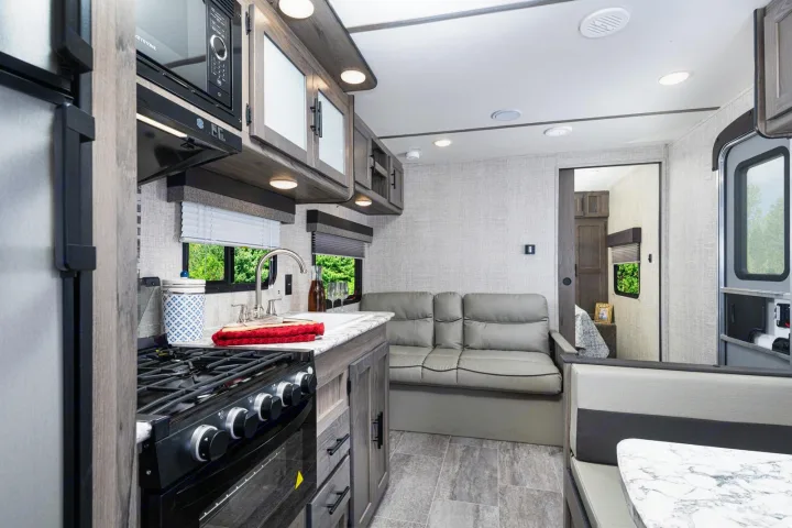 This RV rental interior showcases a modern kitchen, comfortable sofa, dinette, and a peek into the bedroom area.. Gulfstream 26BHG 2022