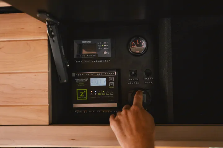 Inside an RV rental, a hand operates the main power, solar charging (13.1V), and water system controls on a van panel.. Mercedes-Benz Sprinter 2021
