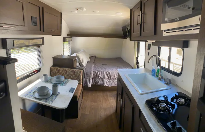 Modern RV rental interior with bed, dining booth, kitchenette featuring sink, stove, and microwave.. Forest River EVO 2020