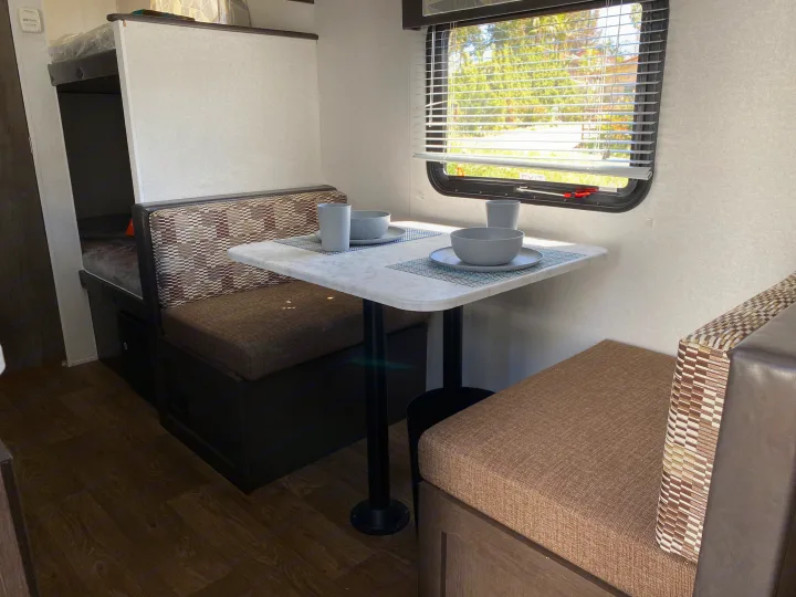 Cozy RV rental interior featuring a bright dinette area with a table and bench seats, plus bunk beds visible in the background.. Forest River EVO 2020
