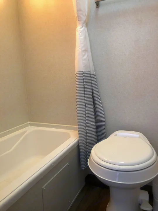 Clean RV rental bathroom featuring a white toilet, bathtub, and striped shower curtain, perfect for comfortable travel.. Forest River EVO 2020