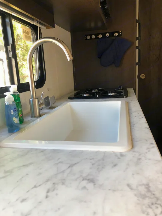 Well-appointed RV rental kitchen with a spacious sink, compact stove, marble counters & hanging oven mitts.. Forest River EVO 2020