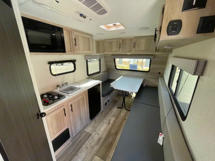 Interior of an RV rental showing a compact kitchenette with stove, sink, microwave, plus a dining area with bench seating.. Sportsmen Classic 2022