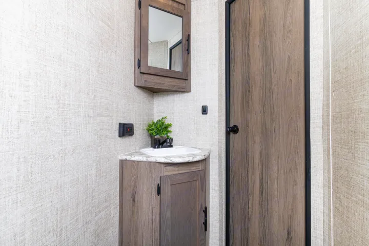 RV rental bathroom showing a corner vanity, sink, overhead medicine cabinet with mirror, and sleek wood cabinet. Light textured walls.. Gulfstream 26BHG 2022