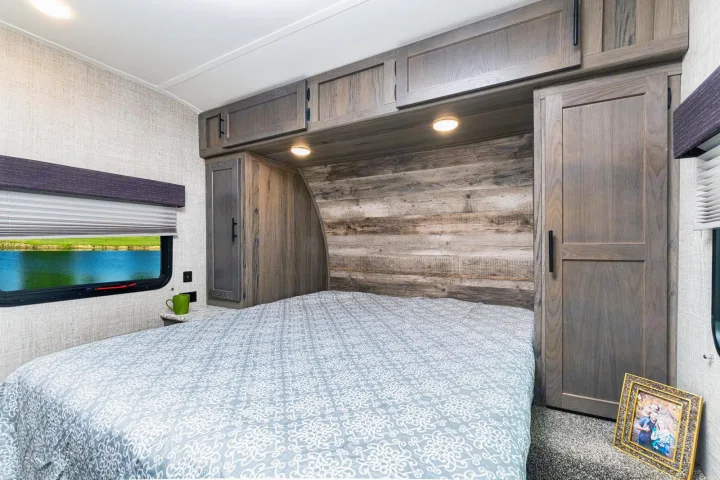 Relax in this cozy RV rental bedroom, featuring a queen bed with patterned bedding, built-in storage, and a scenic lake view window.. Gulfstream 26BHG 2022