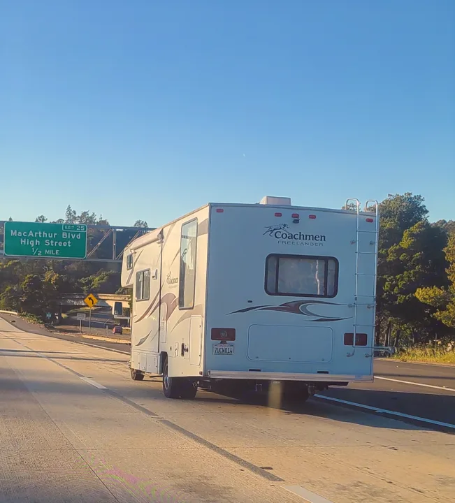 A white Coachmen RV rental on a sunny highway, nearing the MacArthur Blvd exit sign.. Coachmen Freelander 2011