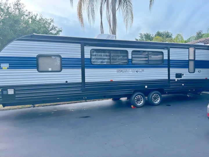 Grey Wolf travel trailer RV rental, grey and blue, parked on a paved lot. Cloudy sky above.. Forest River Cherokee Grey Wolf 2022
