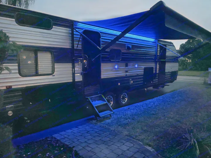This RV rental shines at dusk with vibrant blue LED lighting under its awning and along the ground. Steps lead inside.. Forest River Cherokee Grey Wolf 2022