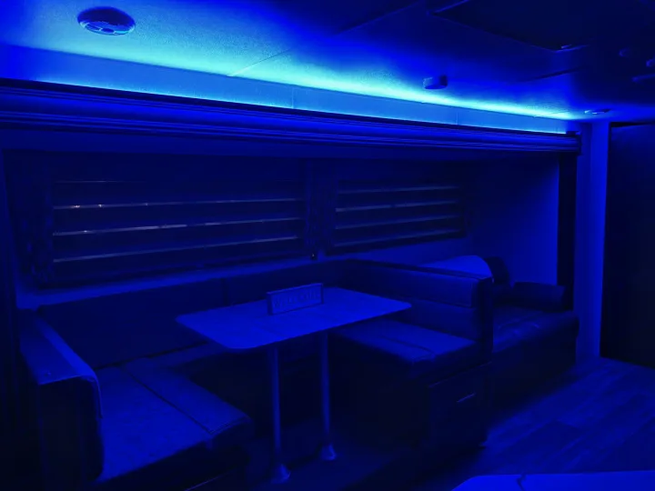 Blue-lit RV rental dinette with U-shaped seating and table, creating a unique ambiance.. Forest River Cherokee Grey Wolf 2022