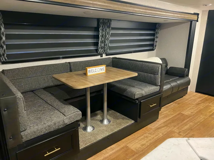 **RV rental** interior: a cozy dinette with booth seating, light wood table, and striped blinds. Perfect for comfort on the road.. Forest River Cherokee Grey Wolf 2022
