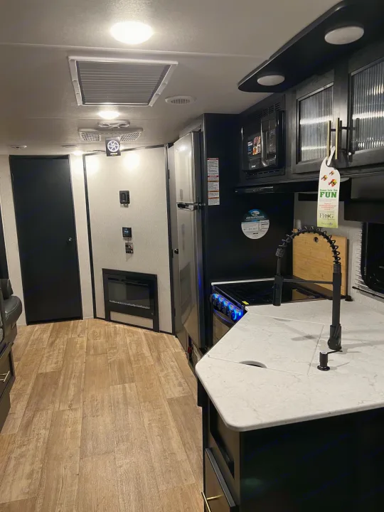 RV rental: modern kitchen with stove, sink, microwave, fridge, and a cozy fireplace visible down the hall.. Forest River Cherokee Grey Wolf 2022