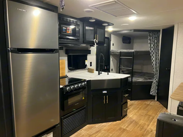 Modern RV rental interior featuring a fully equipped kitchen (fridge, oven, microwave) and cozy bunk beds. Perfect for family adventures!. Forest River Cherokee Grey Wolf 2022