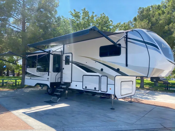 Spacious Paradigm fifth-wheel RV rental parked at a sunny campsite with awnings extended, perfect for luxury camping.. Alliance RV Paradigm 2021