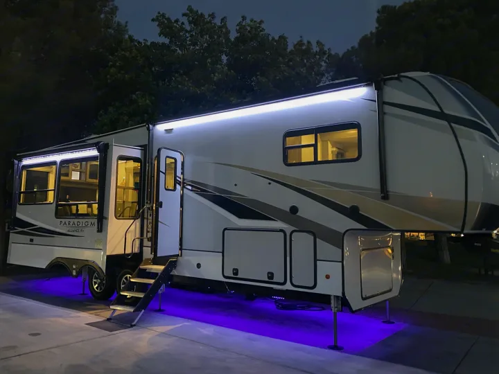 A stylish rv rental, a large white fifth-wheel, glows with bright white awning lights and cool purple underglow at night.. Alliance RV Paradigm 2021
