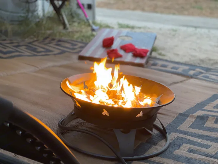 A glowing fire pit provides warmth for an evening at an RV rental campsite, with a US flag cornhole board in the background.. R-Vision Trail-Lite Trail-Cruiser 2004