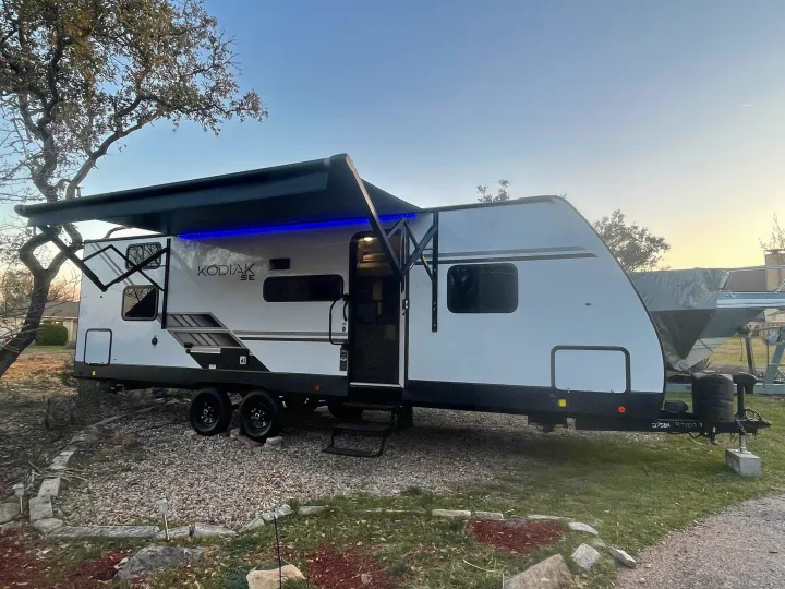 A Kodiak SE travel trailer, ideal for an RV rental, is parked outdoors with its blue-lit awning extended.. Dutchman Kodiak SE 2022