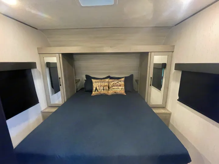 Comfortable RV rental bedroom featuring a queen bed with adventure pillows, mirrored wardrobes, and blackout blinds.. Dutchman Kodiak SE 2022
