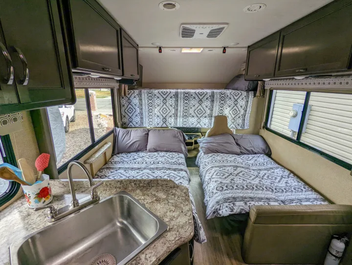 Spacious RV rental interior featuring twin beds with patterned bedding, a functional kitchen sink, and ample overhead storage.. Thor Four Winds 2020