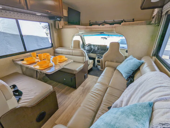 RV rental interior: A fully equipped dinette with orange place settings, a cozy sofa with pillows, and the driver's cabin visible.. Thor Four Winds 2020